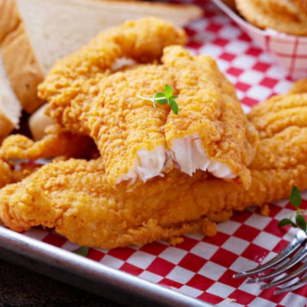 Crispy fried fish fillets with a sprig of thyme on red and white checkered paper.