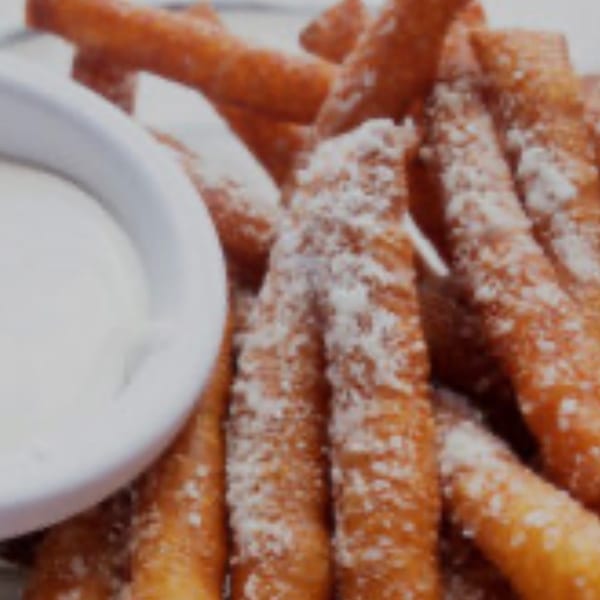 Sweet potato fries dusted with powdered sugar, served with a side of white dipping sauce.