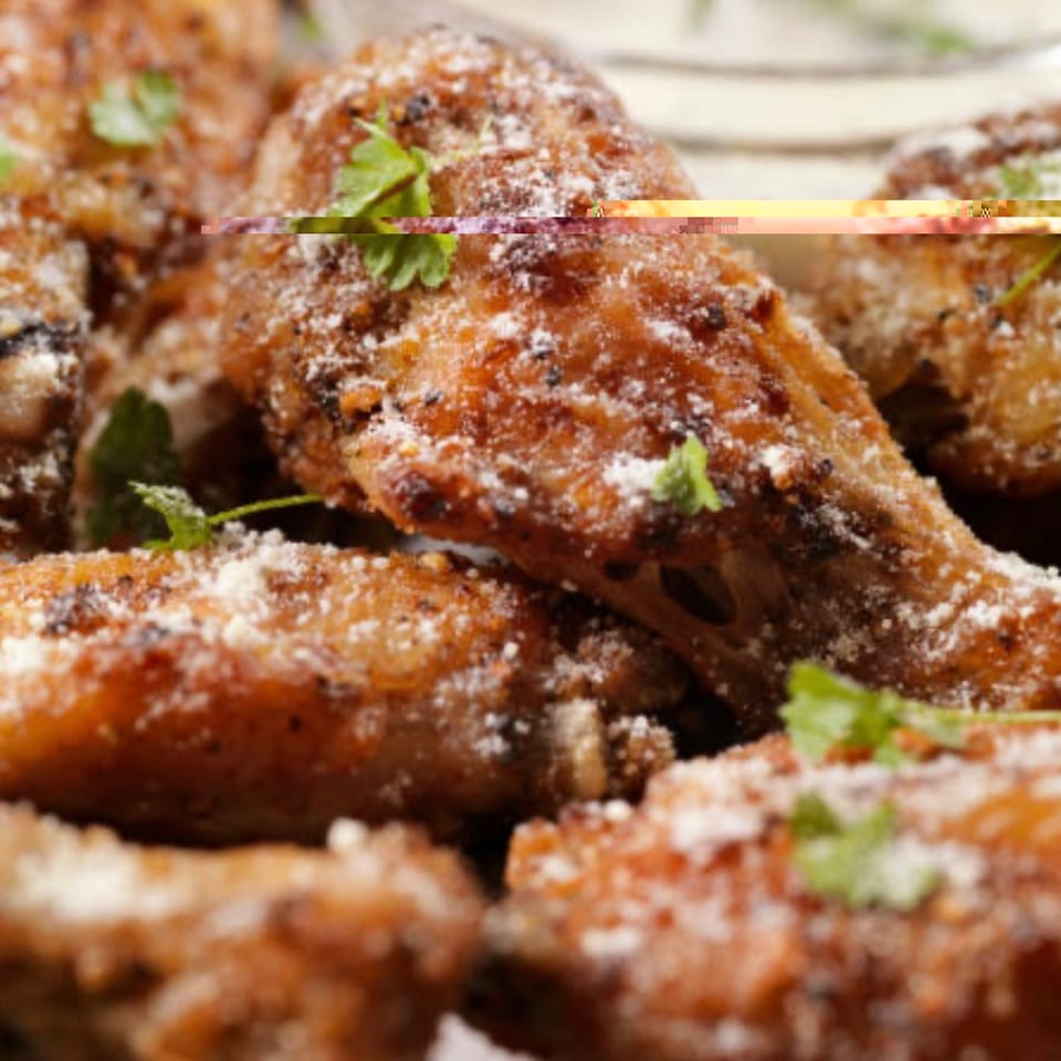 Close-up of crispy fried chicken wings dusted with white powder and garnished with fresh parsley.