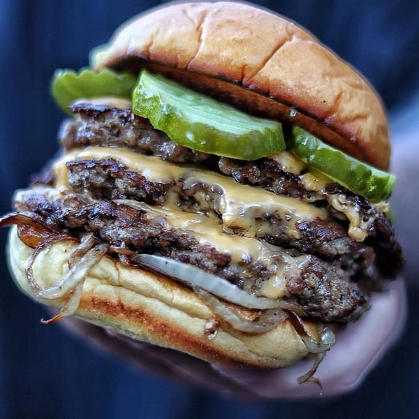 A double patty burger with melted cheese, caramelized onions, and pickles on a toasted bun.